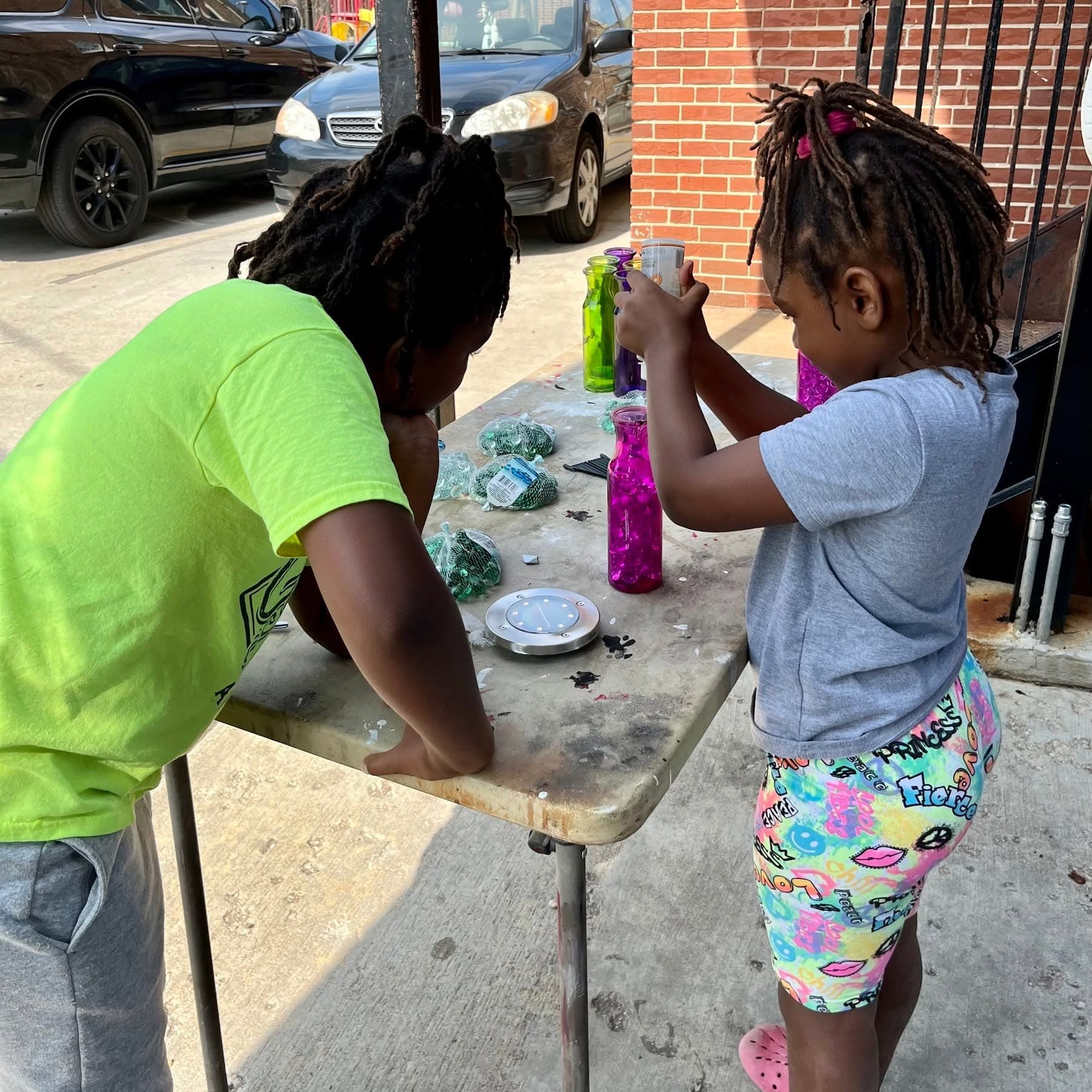 Two girls make a craft together at a folding table outdoors