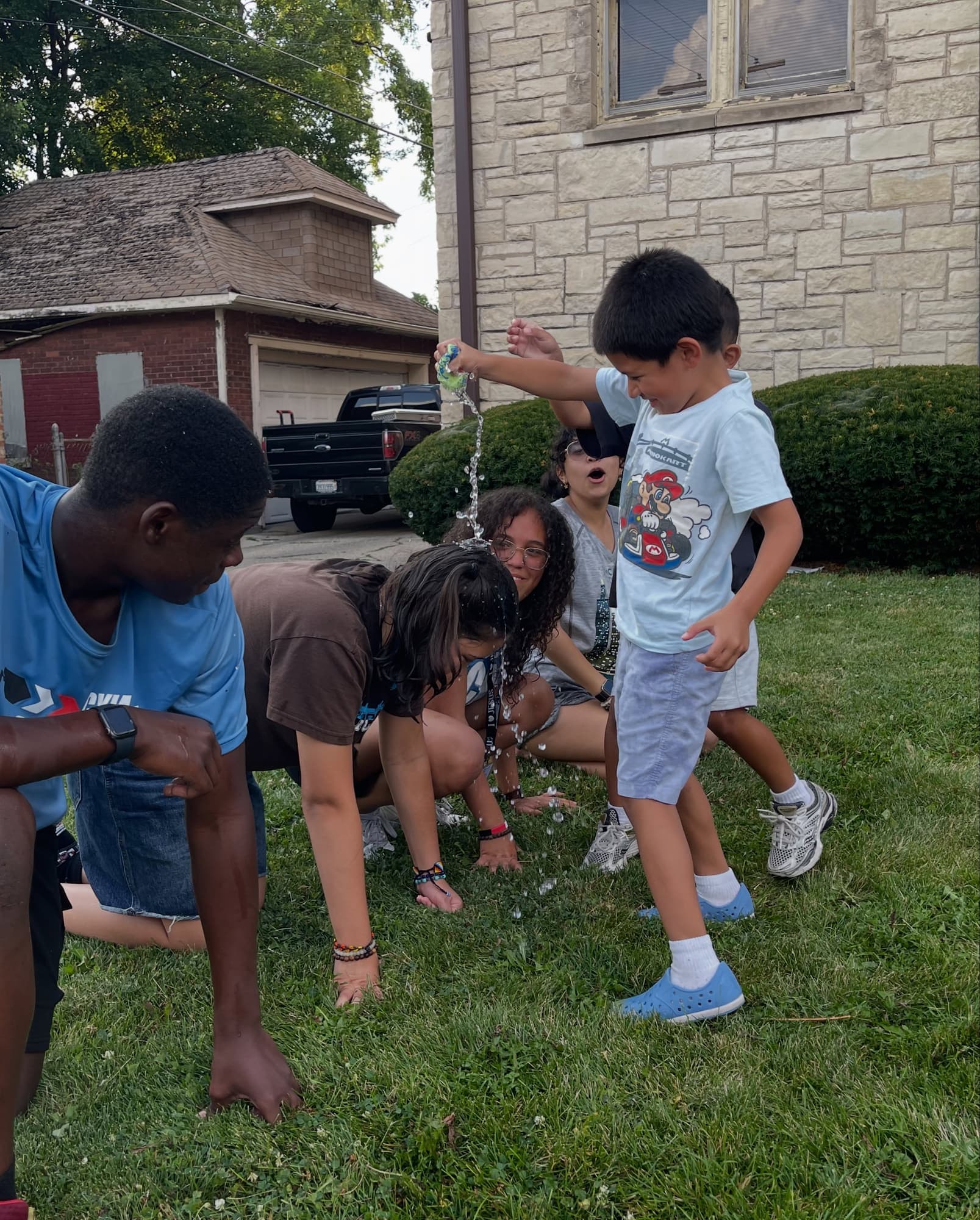 Children and a leader crouch on a lawn beside a stone church during a game