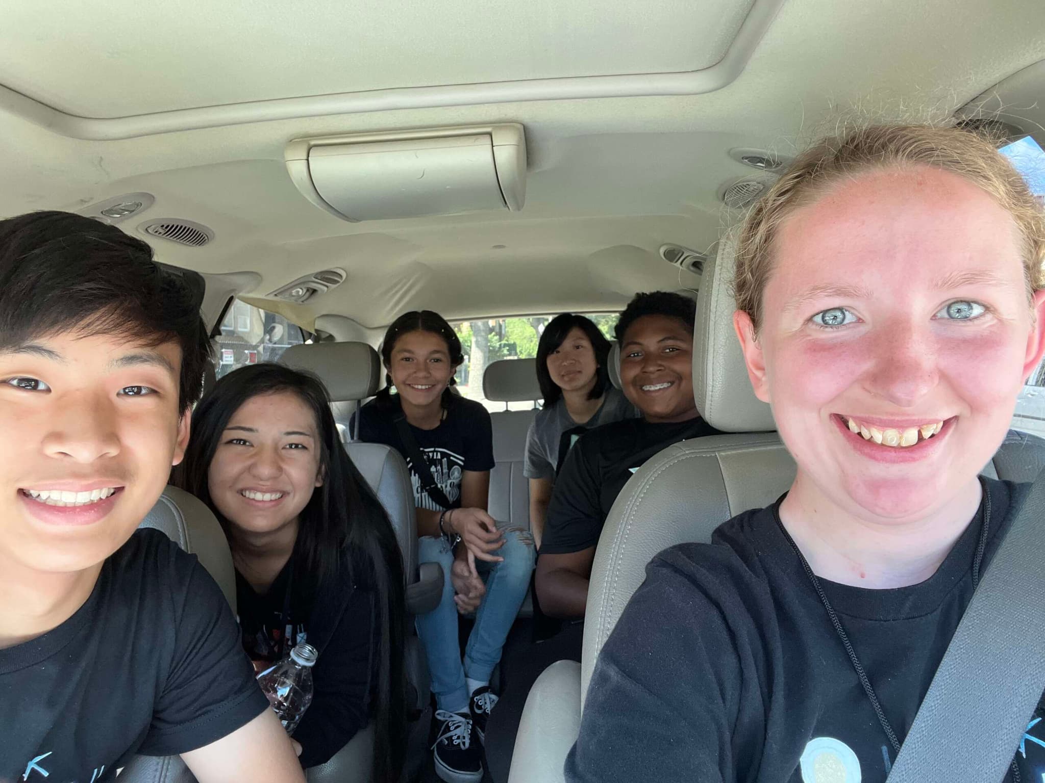 Five young people in matching black shirts smile from the seats of a van